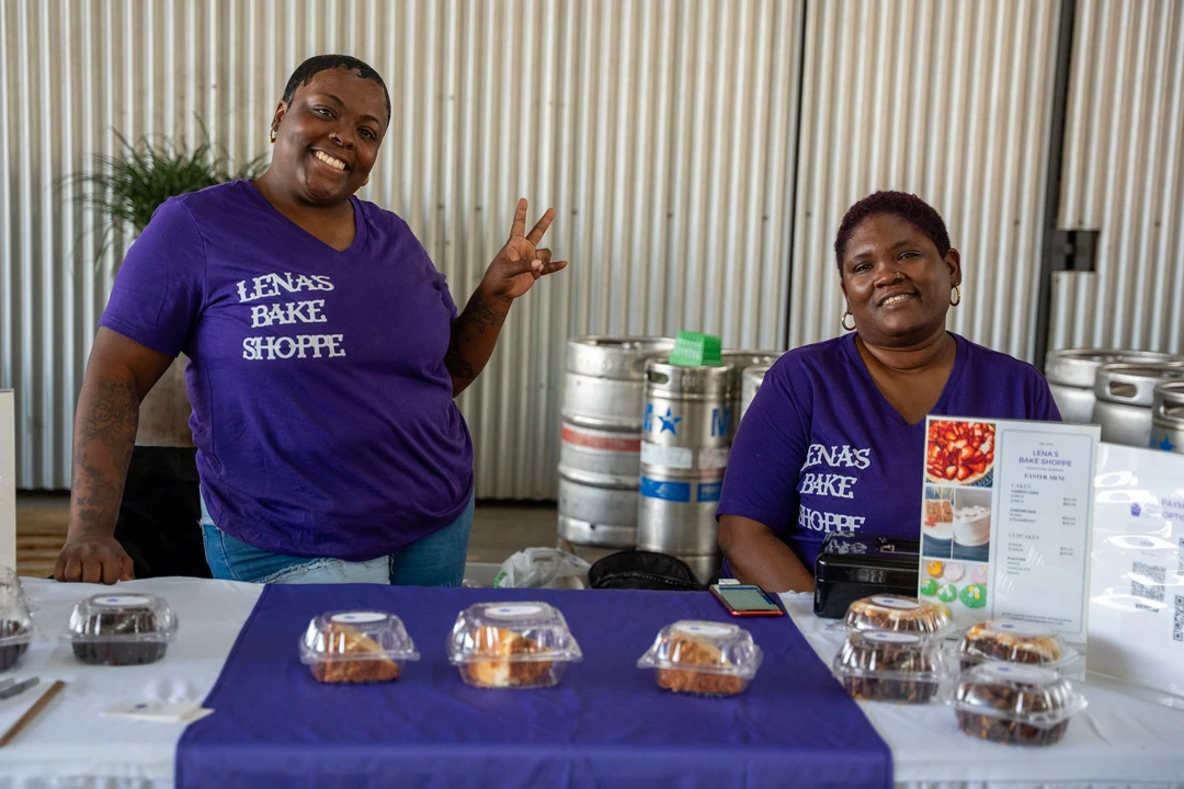 Two bakers standing behind a purple bake-shop table.