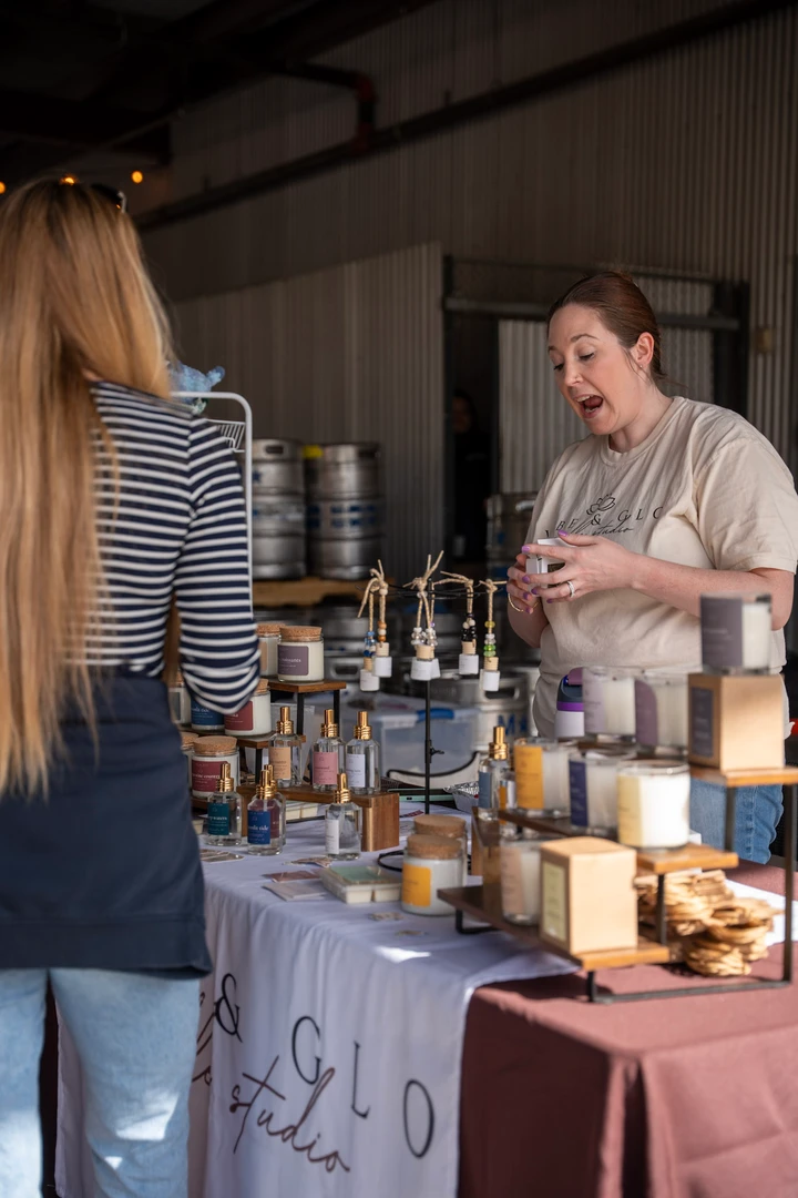 A maker behind a table of jars and handmade goods.