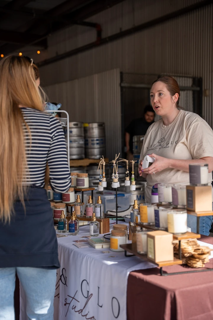 A maker behind a table of jars and handmade goods.